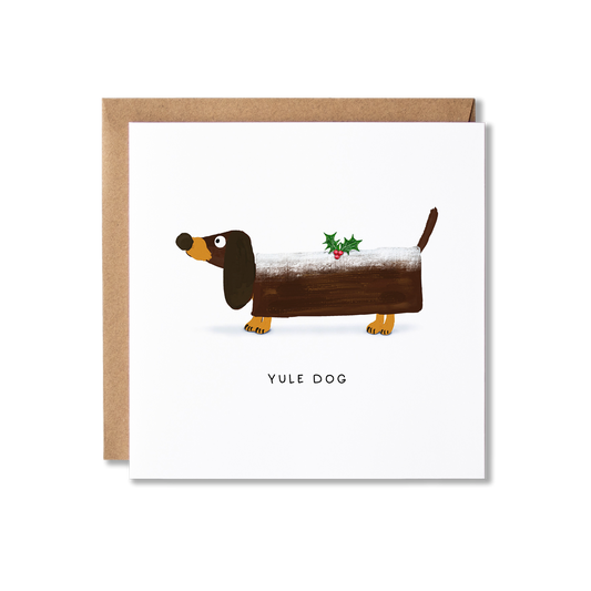 Christmas card with illustration of a Dachshund sausage dog wearing a log shape that looks like a Yule log with a spring of holly on top and the message Yule Dog.